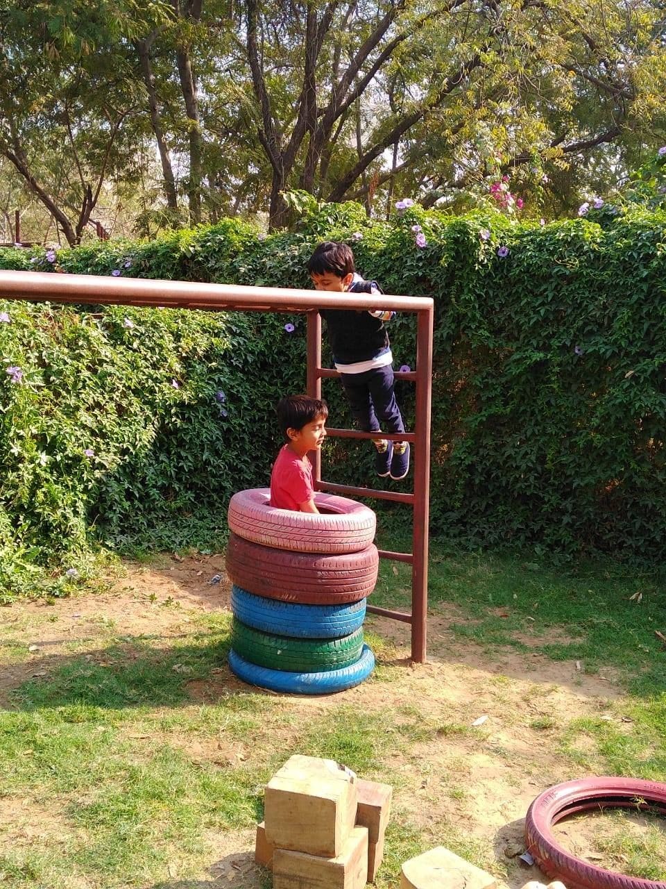 Children playing on a jungle gym with stacked colorful tires in a garden surrounded by green foliage.